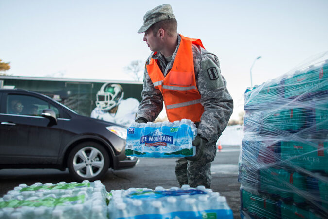an Army National Guard specialist, in uniform, loading pallets of bottled water into cars