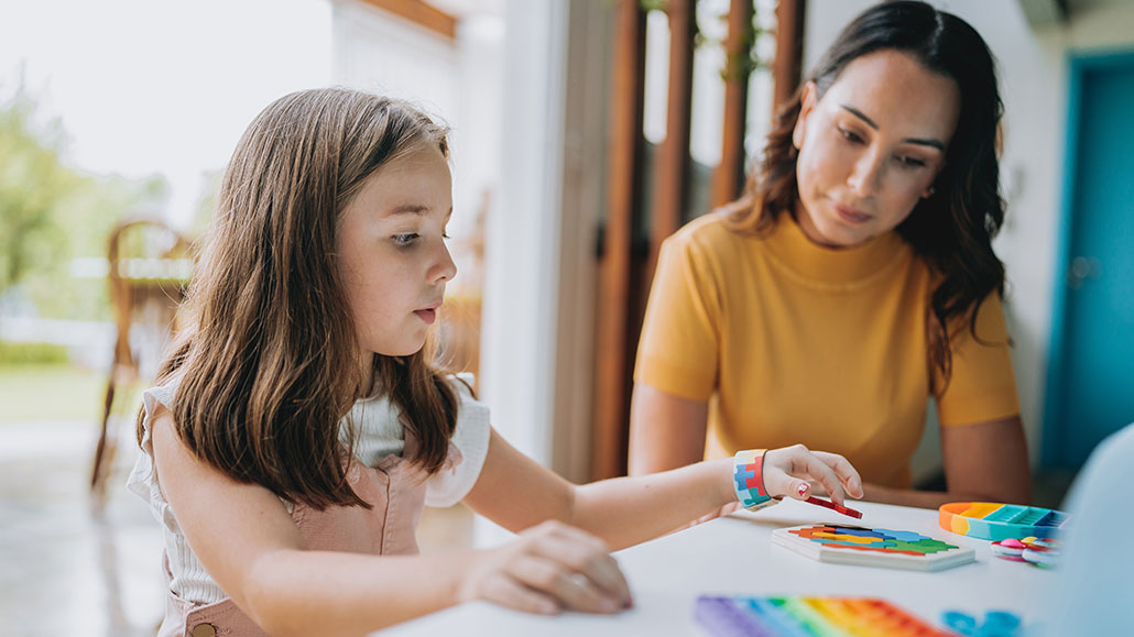 a girl and her mom sit a table in a restaurant, the girl is playing with various rainbow colored fidget toys