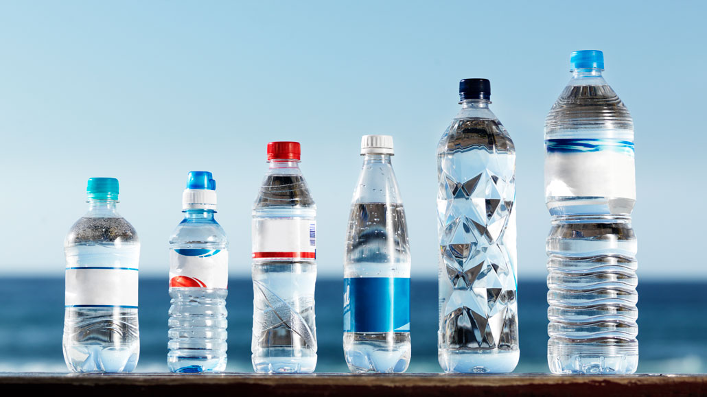 a row of single use water bottles on a wood plank in front of a beach