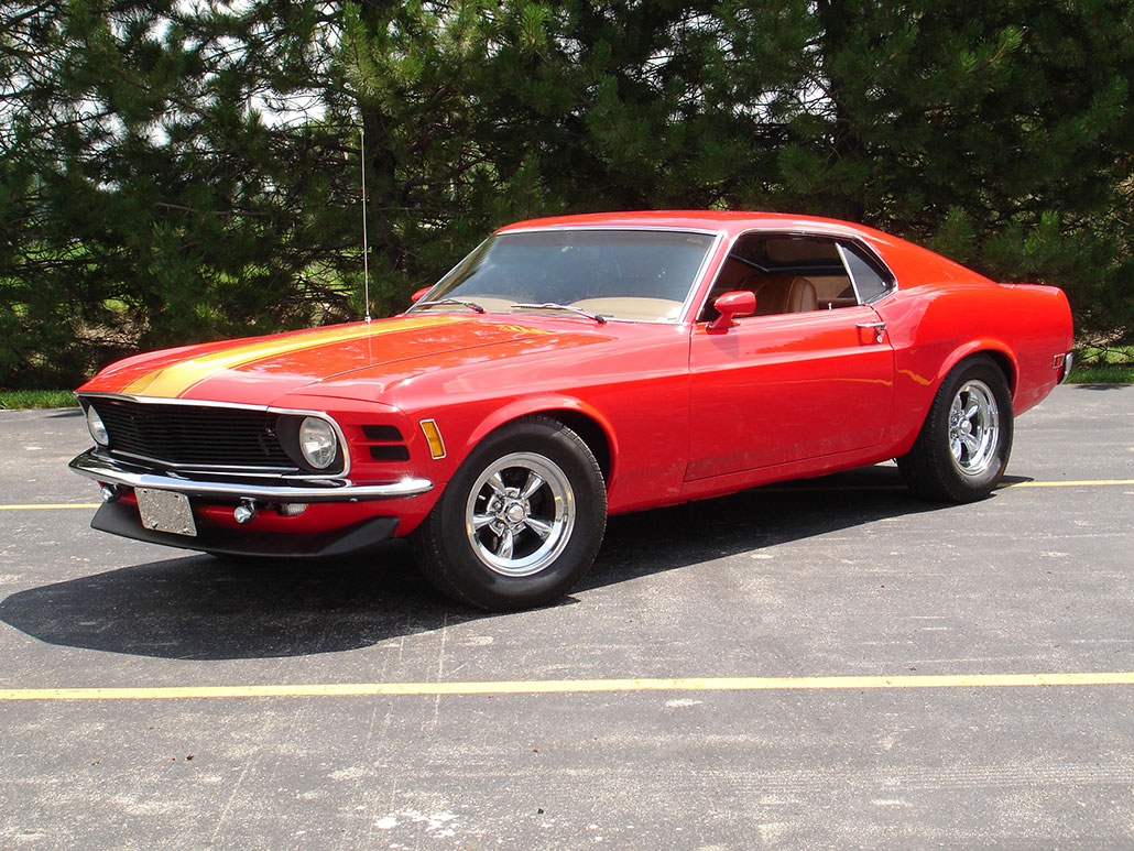 a red-orange muscle car from the 1970s parked outside