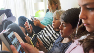 a photo of a row of kids sitting on a sofa, all of them are on devices