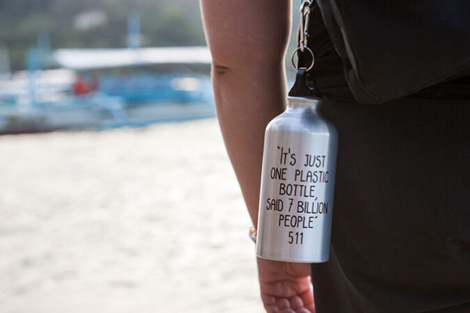 a reusable metal water bottle hanging of of a person's bag