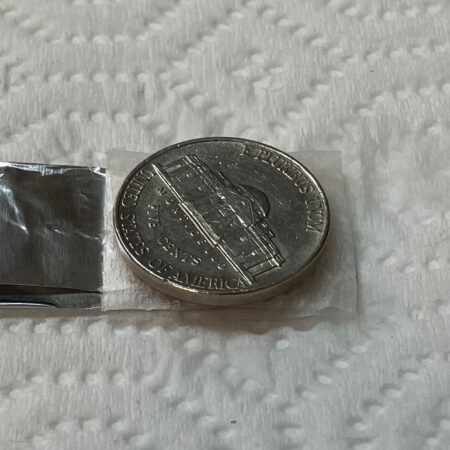 a nickel sits atop a damp piece of paper towel, which covers a penny sitting atop a piece of aluminum foil atop a dry paper towel