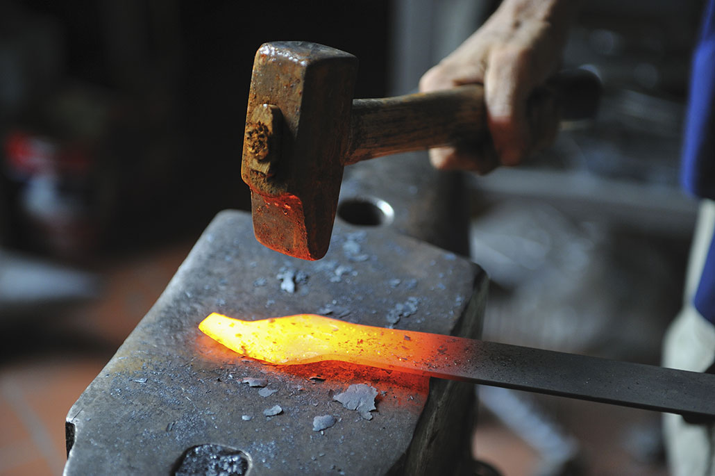 a blacksmith hammer pounding a strip of red-hot metal on an anvil