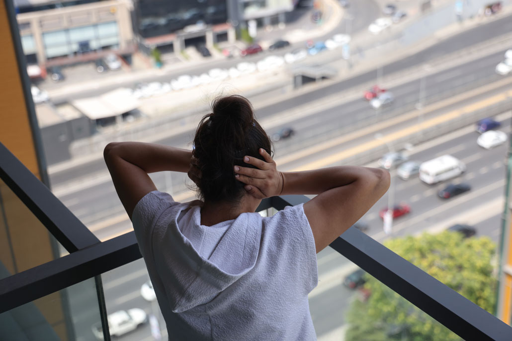 a person stands on a balcony overlooking a highway, they are covering their ears and looking down and away