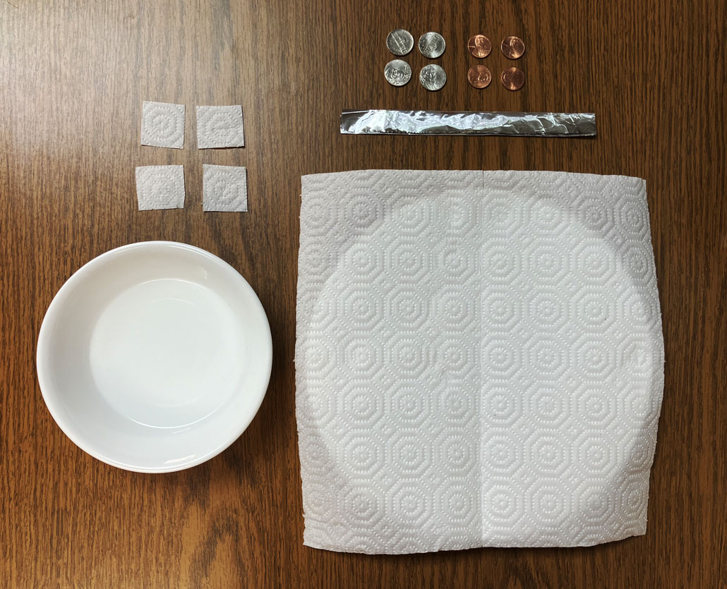 A few pennies and nickels, small paper-towel squares, a vinegar-salt solution and an aluminum strip are all laid out on a desk