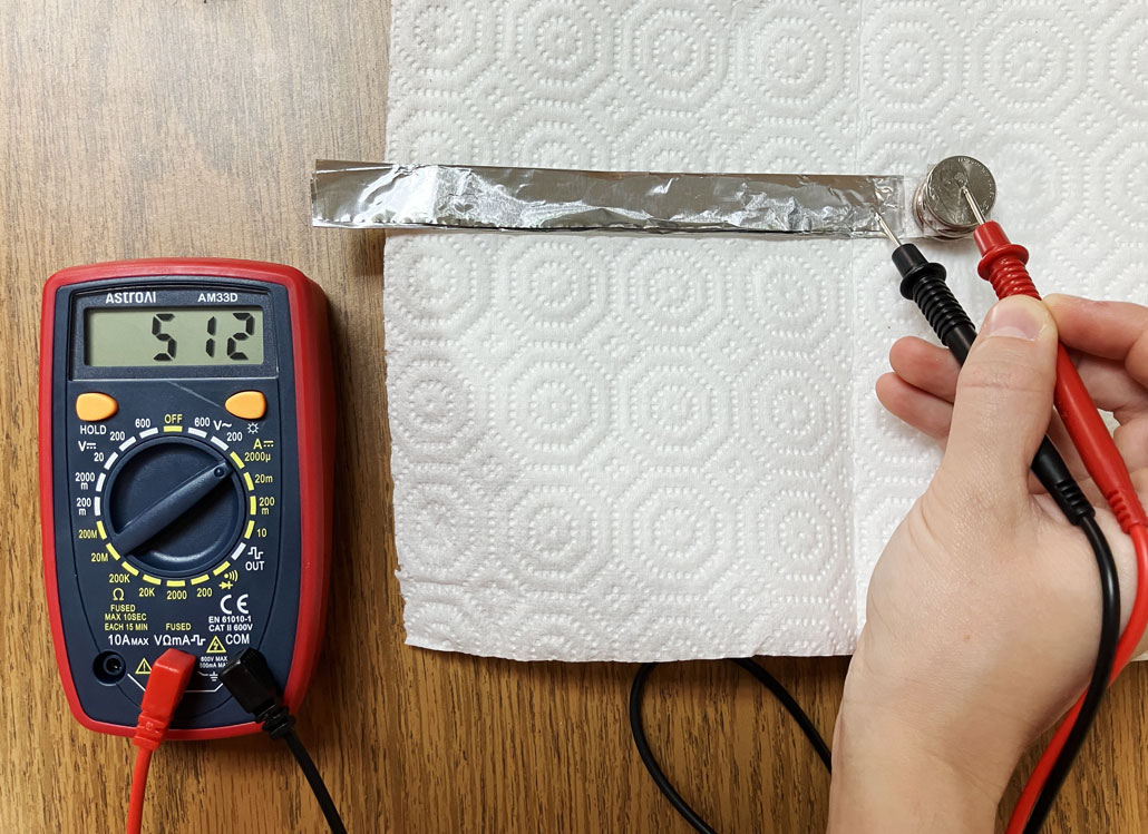 a hand holds the two leads of a multimeter to the top and bottom of a voltaic stack made out of coins