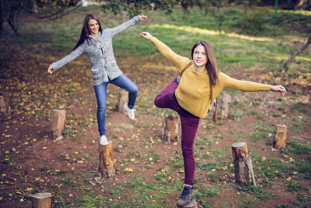 two girls balancing on logs placed vertically 