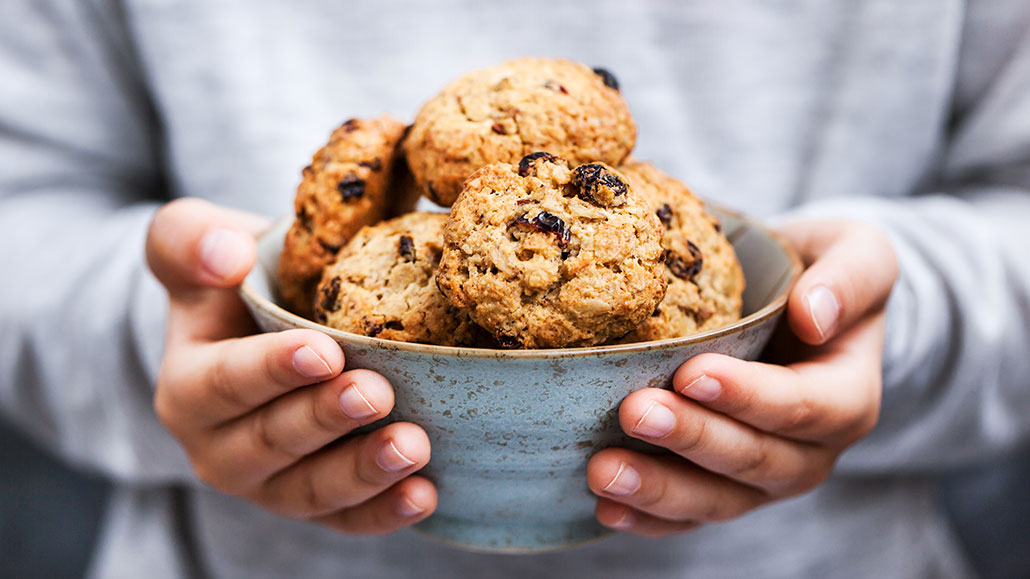 a person's hands holding large chunky oatmeal raisin cookies in a clay bowl