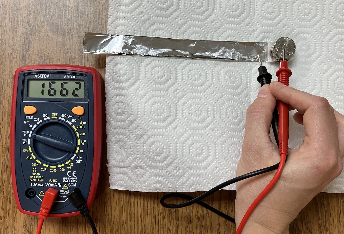 a hand holds the two leads of a multimeter to the top and bottom of a voltaic stack made out of coins