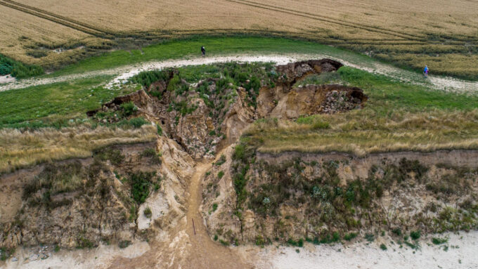 a coastal landslide drags a river of water and soil down a hill from farmland to the beach
