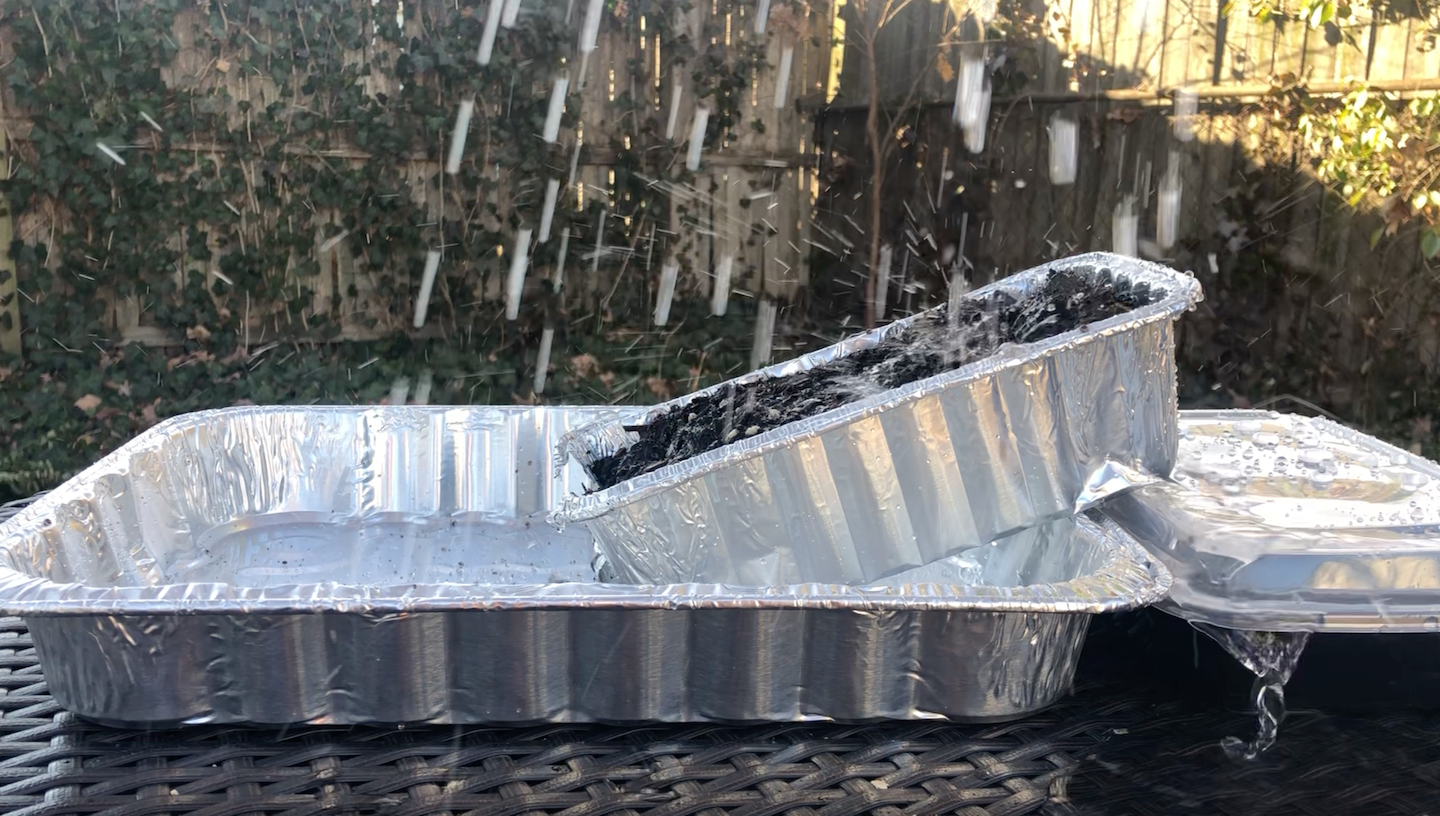 a watering can (out of frame) pours water down onto a cake pan filled with water so that water droplets cover the whole pan