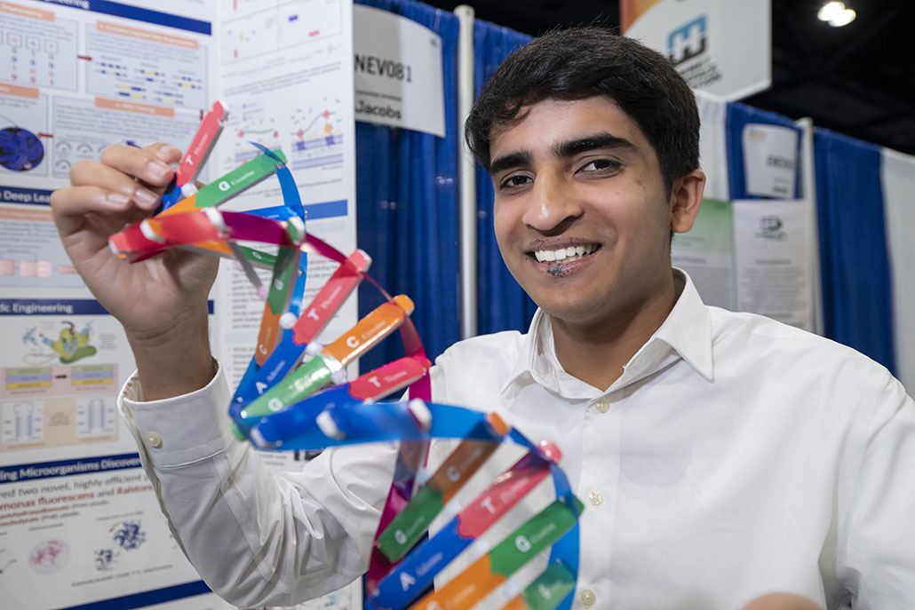Krish Pai at Regeneron ISEF 2024. He is standing next to his project board and holding a model of a DNA strand.