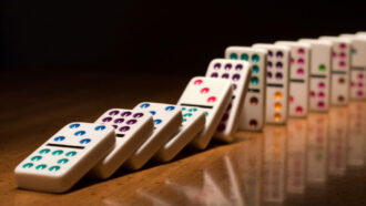 a series of dominos lined up on a desk is starting to tumble after the first has been knocked over
