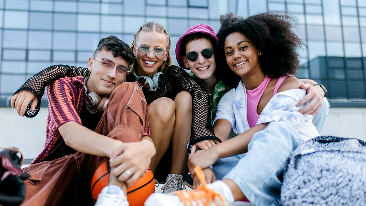a groupd of teens sitting outside a glass windowed building, the teens look young and happy