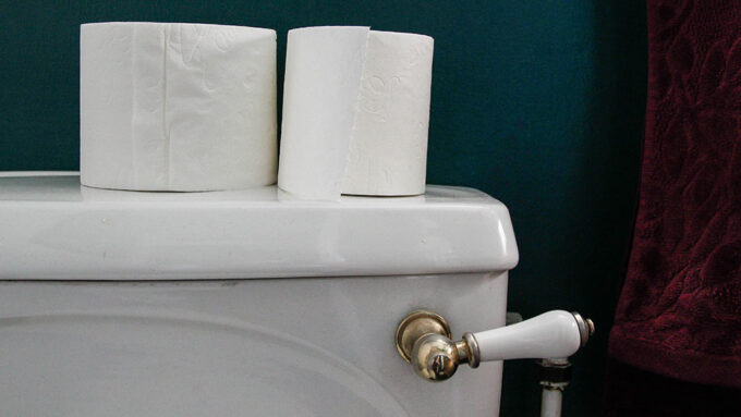 two rolls of toilet paper on the top of the water tank of a toilet, a fancy flush handles is also visible