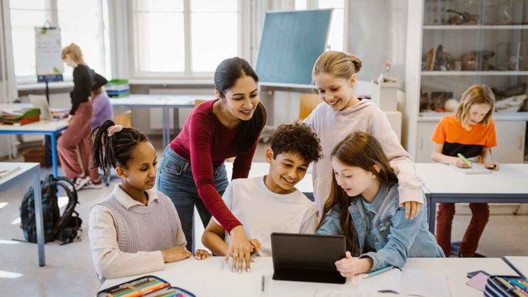 a teacher leans over a table where students are working together happily