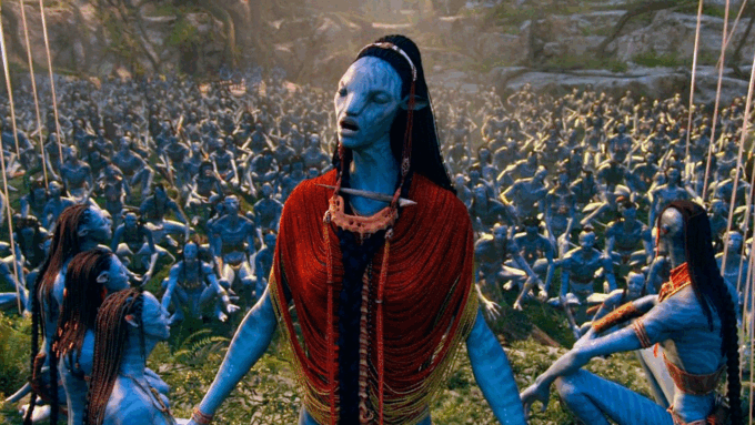 A blue Na'vi humanoid alien from Avatar closes her eyes as she sings in front of a gathered crowd of Na'vi sitting on the ground behind her