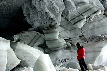 a person standing in front of an area of a glacier where layers of ice can be seen
