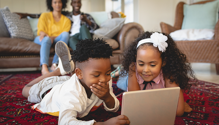 a family picture with parents on a sofa and two kids lying on the floor using a laptop