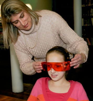 Researcher Mariana Figueiro of Rensselaer Polytechnic Inst. helps a middle school student test a pair of orange goggles in an early study showing the connection between sleep problems and lack of exposure to morning light. Credit: Lab of Mariana Figueiro/ RPI