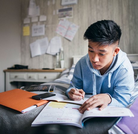 a photo of a young asian man studying his notes while lying in bed