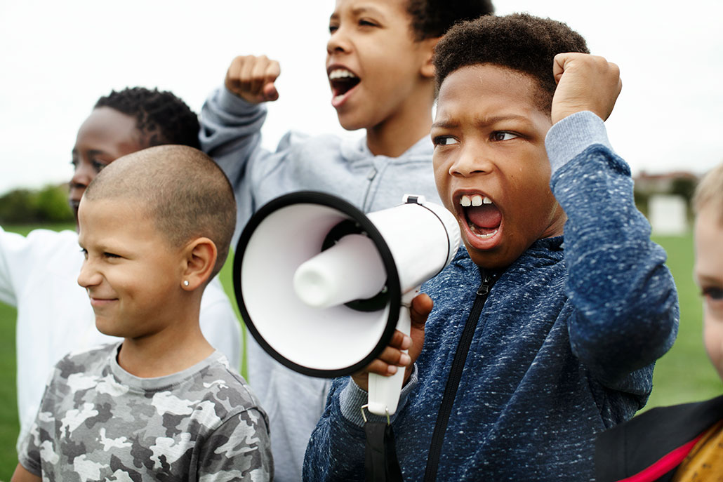 a photo of a young Black teen shouting into a megaphone at a protest
