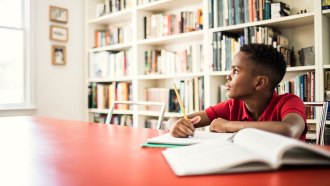 a photo of a boy sitting at a table in a library and daydreaming