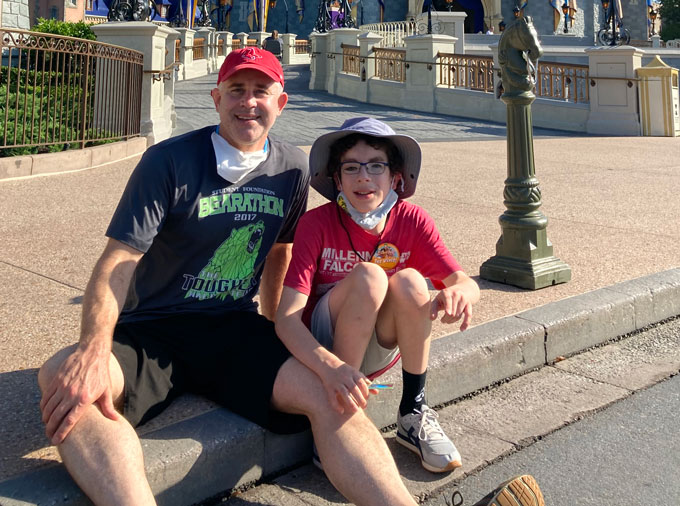 Brian Shaw and his son Noah, sitting on a curb outside, smiling at the camera