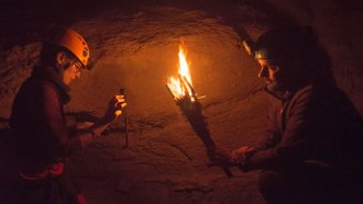 two researchers, one holding a torch in a dark cave