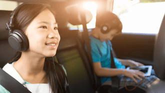 A girl sitting in a car next to her brother listening to headphones
