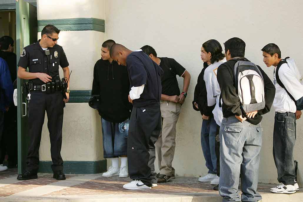 Black and Latino teens stand outside a school building waiting for a police officer to let them in