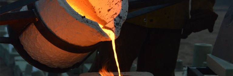 bright orange molten iron being poured from a melting vat into a casting mold