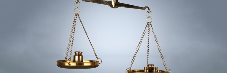 a picture of a brass metal balance scale, one each side are metal weights. One side is lower than the other side. There are also metal weights in front of the scale arranged from largest to smallest.