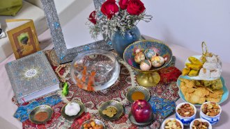 a table is colorfully decorated with items such as bowls of nuts, plates bearing an apple, coins, garlic and powders, as well as an ornate book and mirror