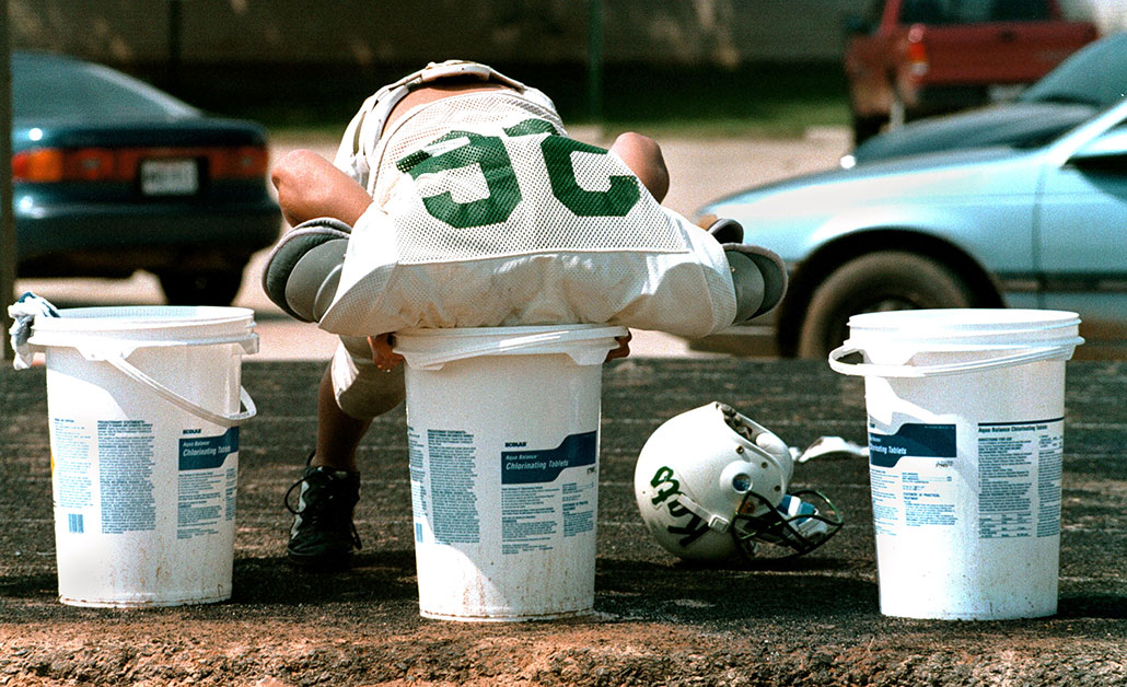 a teen footbal player plunges his head in ice water during football practice