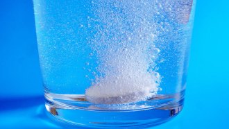 a photo of an Alka-Seltzer tablet starting to fix at the bottom of a clear glass full of water