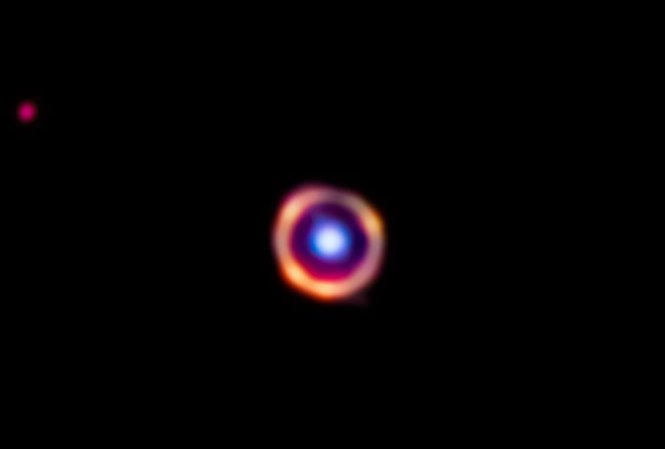 A galaxy 12 billion light- years away and shown is false color is being magnified by a nearer galaxy.