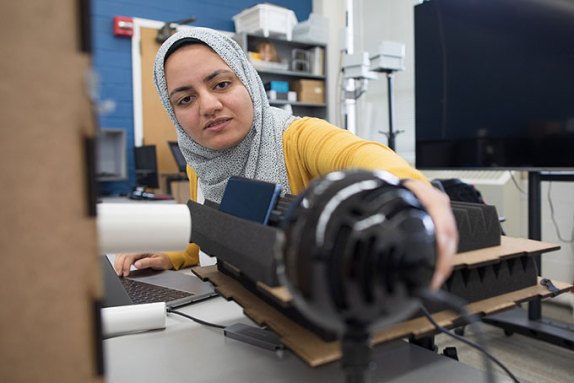a photo of Shimaa Ahmed, a light brown skinned woman wearing a pattened headscarf, looking at the microphone and apparatus