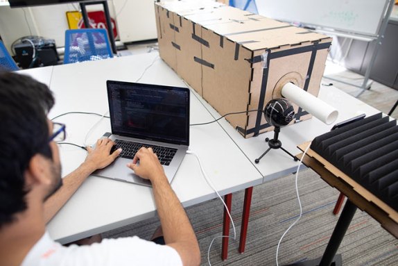 a researcher on a laptop next to the plastic tube device