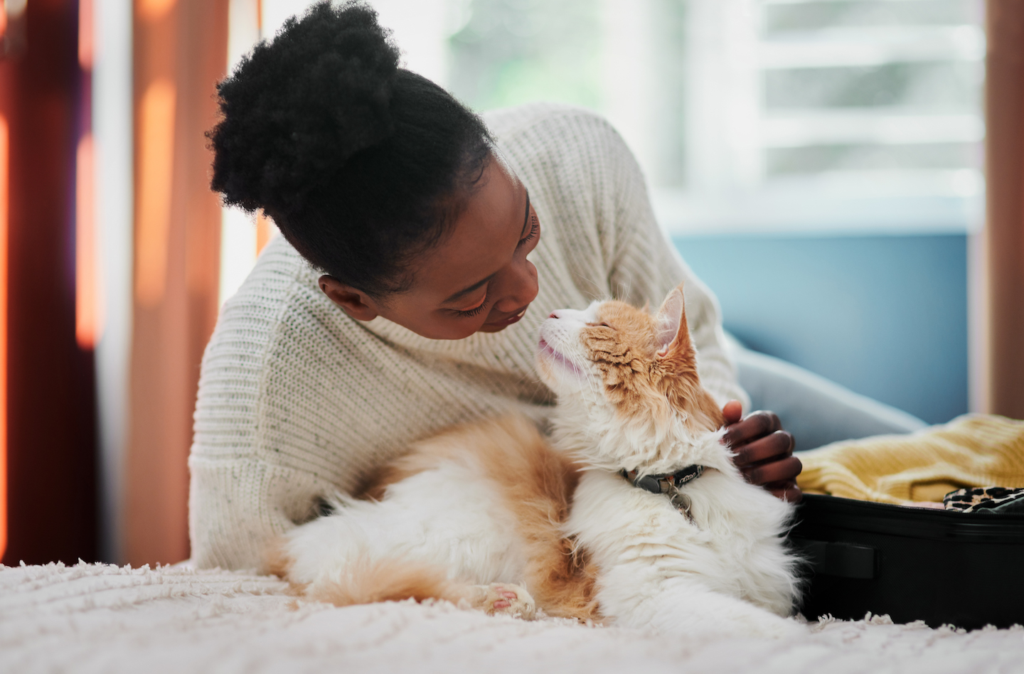 a young woman cuddles up to a white and brown cat on a bed, holding her nose close to the cat's nose