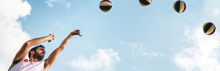 a composite photo showing a guy shooting a basketball in an arc, the basketball is shown four times in consecutive positions, showing the shape of the arc