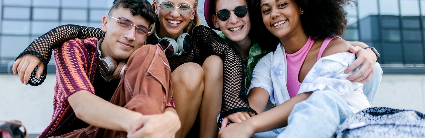 a groupd of teens sitting outside a glass windowed building, the teens look young and happy