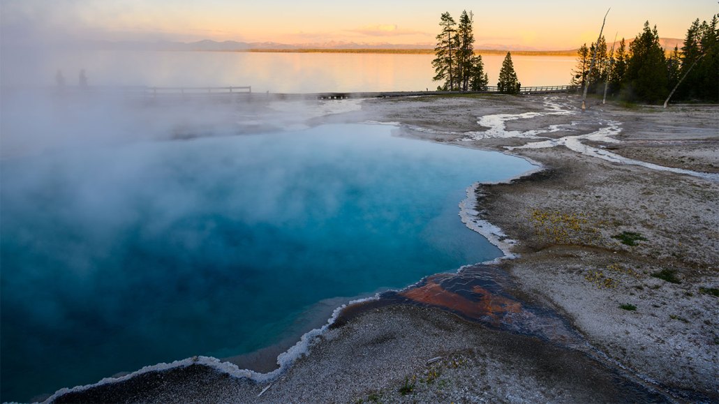 a clear pool of water with crystals at the edges is steaming as the sun sets