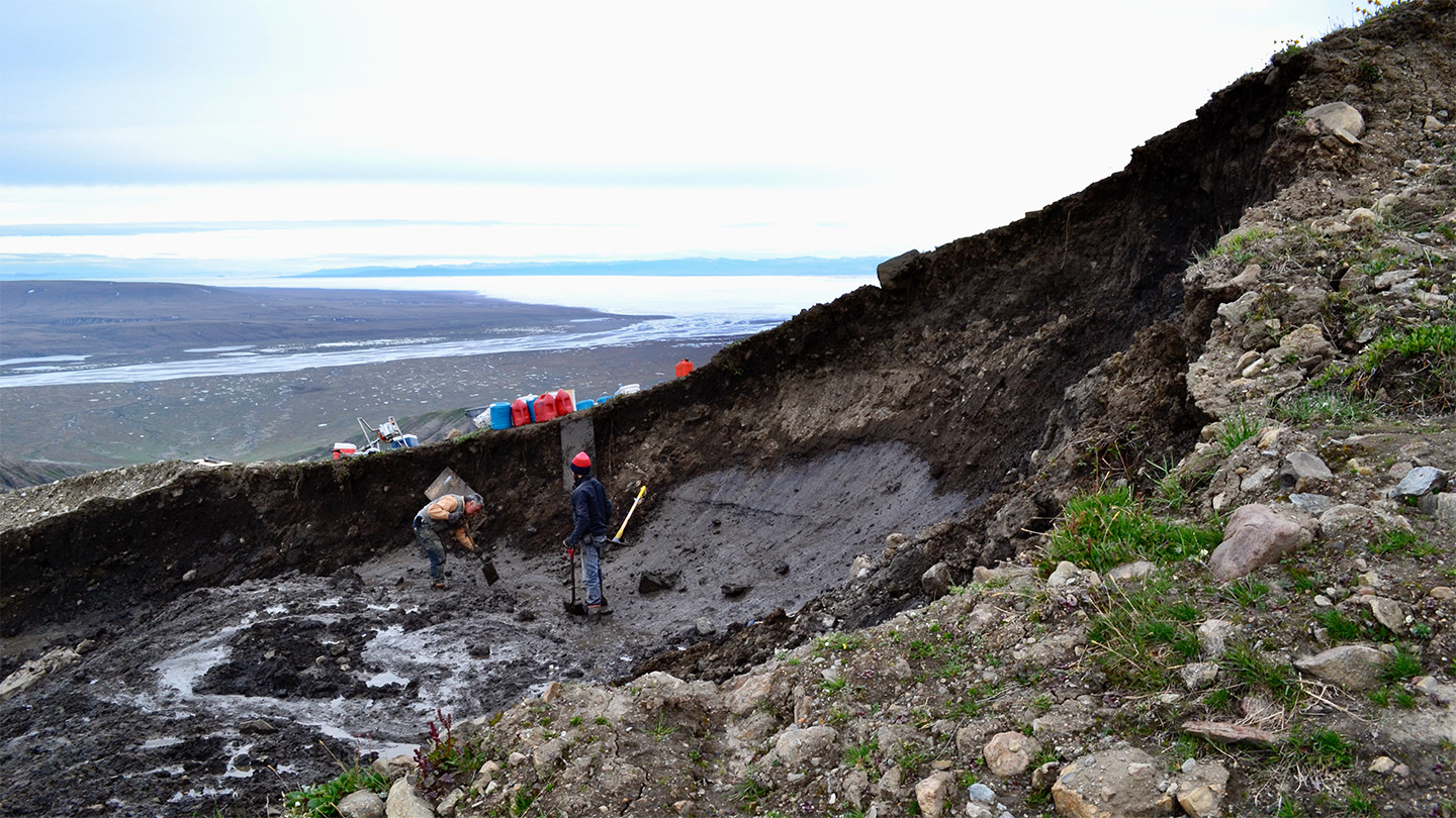 Researchers are shown standing on a patch of exposed glacier ice, amid a landslide slump.
