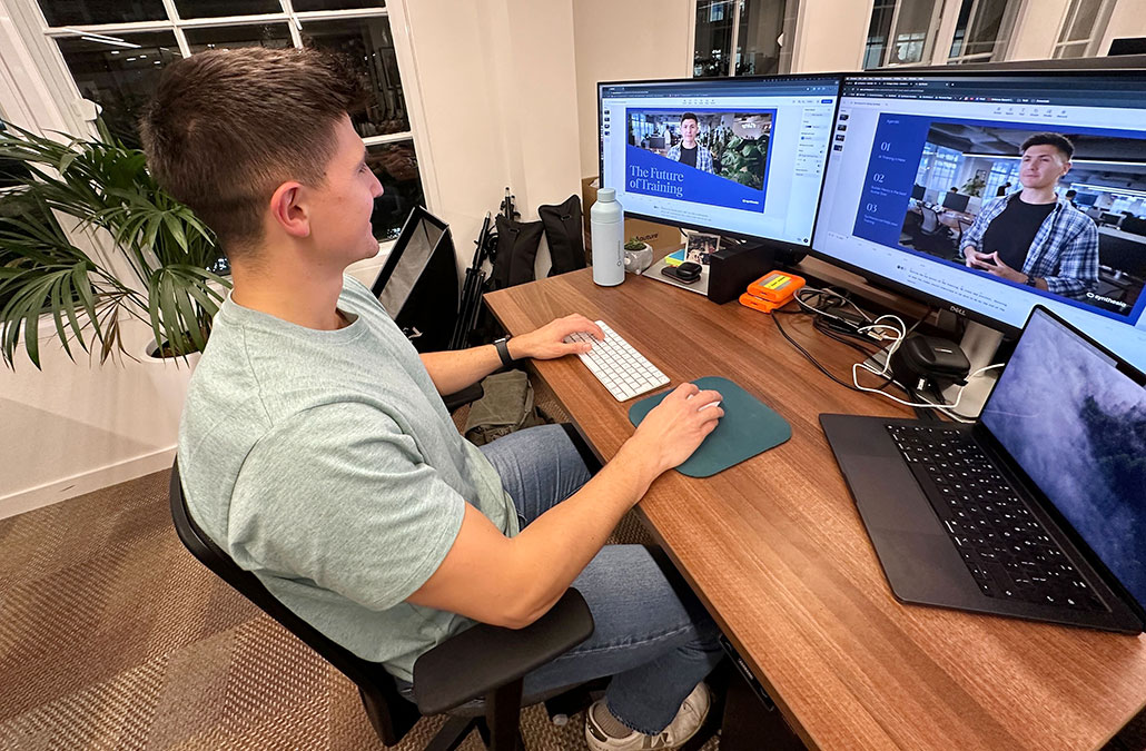 a man sits at a desk and watches his virtual avatar AI double in a video