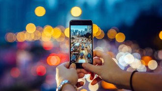 a photo of a cell phone taking a photo of a highway overpass (looking down at traffic) at dusk. The image on the phone is in focus, but the surroundings are out of focus.