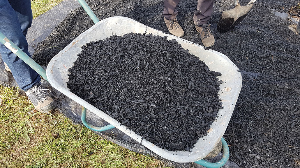 a wheelbarrow full of dark black biochar, almost resembling mulch