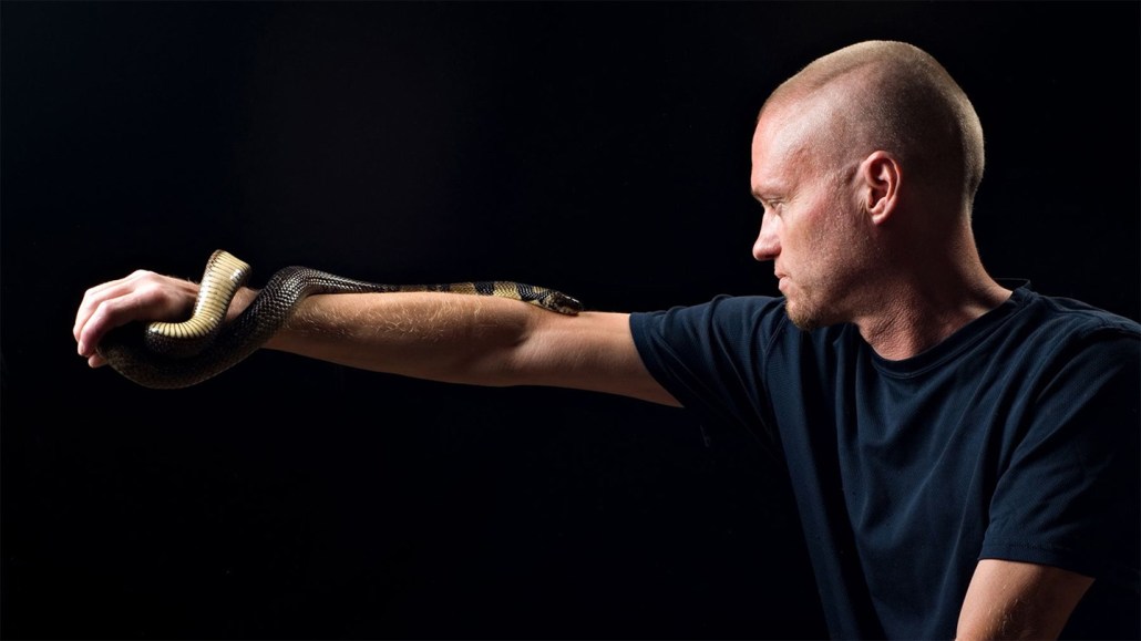 Tim Friede stands in the light with a snake on his arm; his blood was used to make an antivenom cocktail