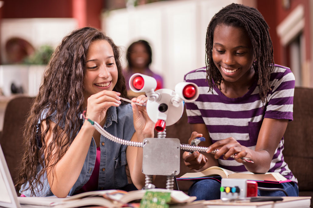 two teen girls work on a robot in a school 